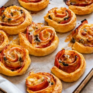 Freshly baked puff pastry ham and cheese pinwheels on the baking tray.