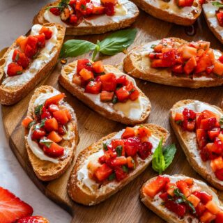 Strawberry bruschetta with fresh basil leaves on a wooden tray.