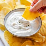 Julia's hand dipping potato chip in creamy chip dip.