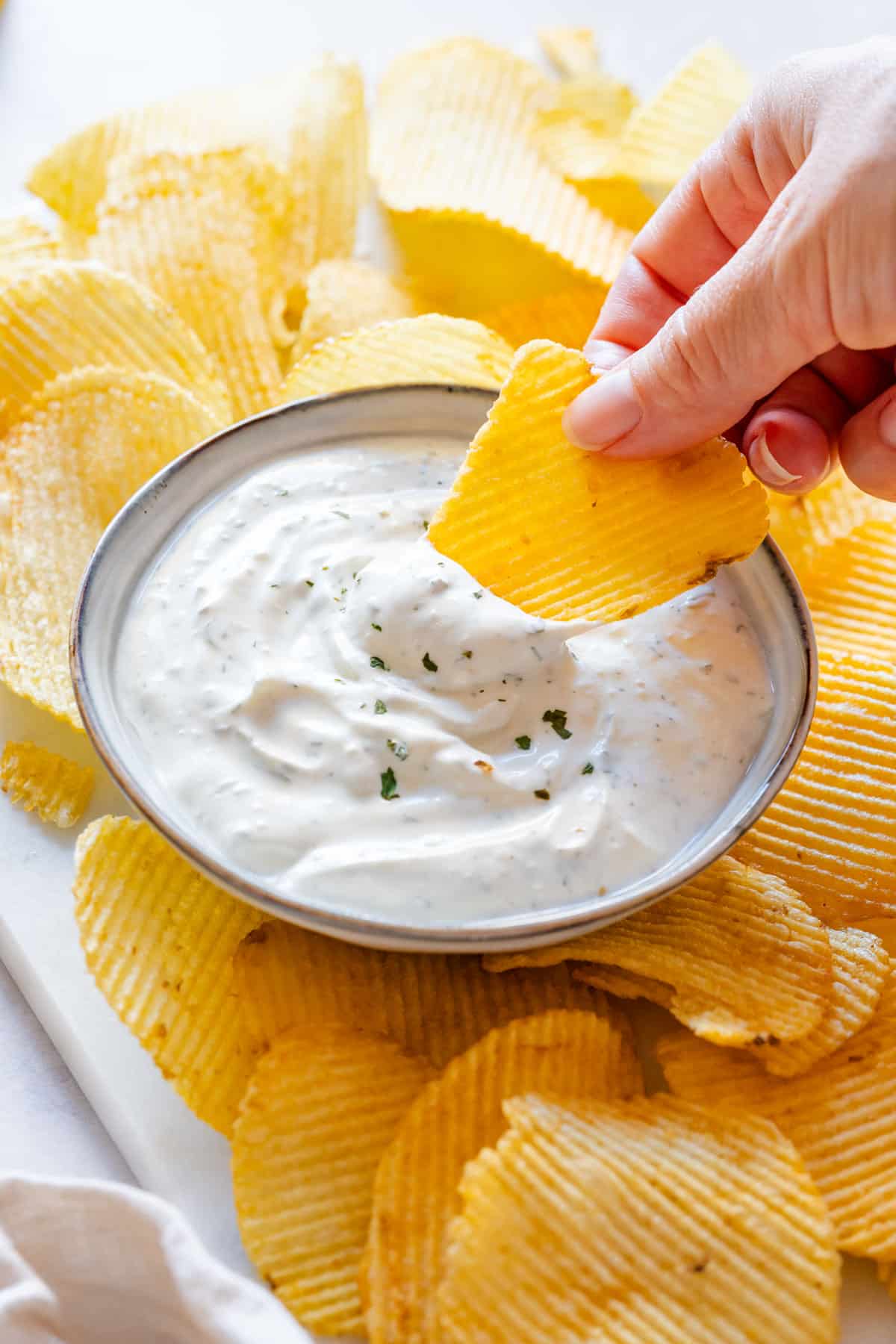 Julia's hand dipping potato chip in creamy chip dip.