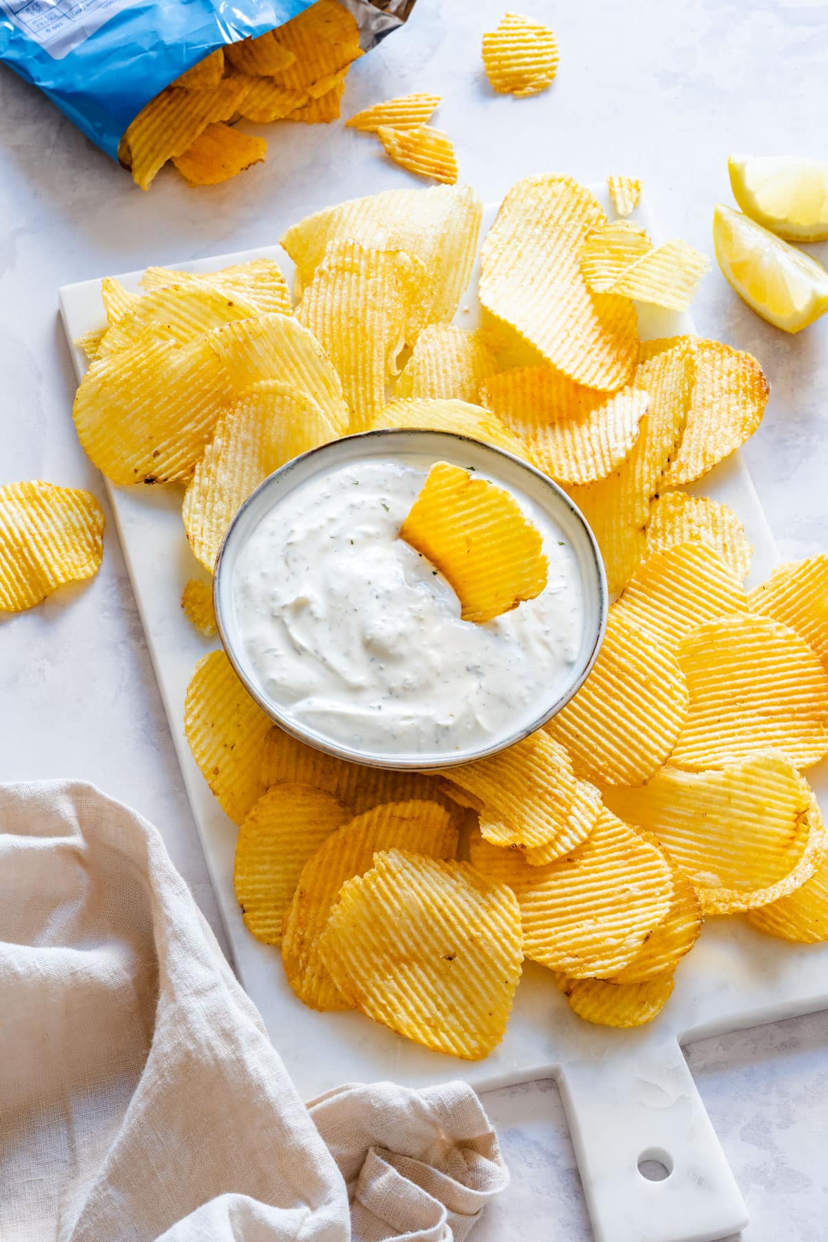 A bowl of creamy white chip dip with potato chips around it.