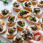 Julia's hand taking a crostini topped with sauted mushrooms.