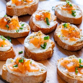 Smoked salmon crostini with cream cheese and dill on wooden serving tray.