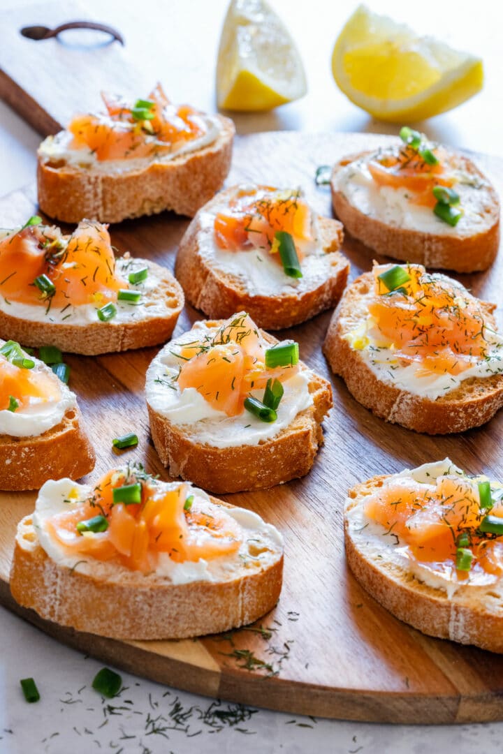 Smoked salmon crostini with cream cheese and dill on wooden serving tray.