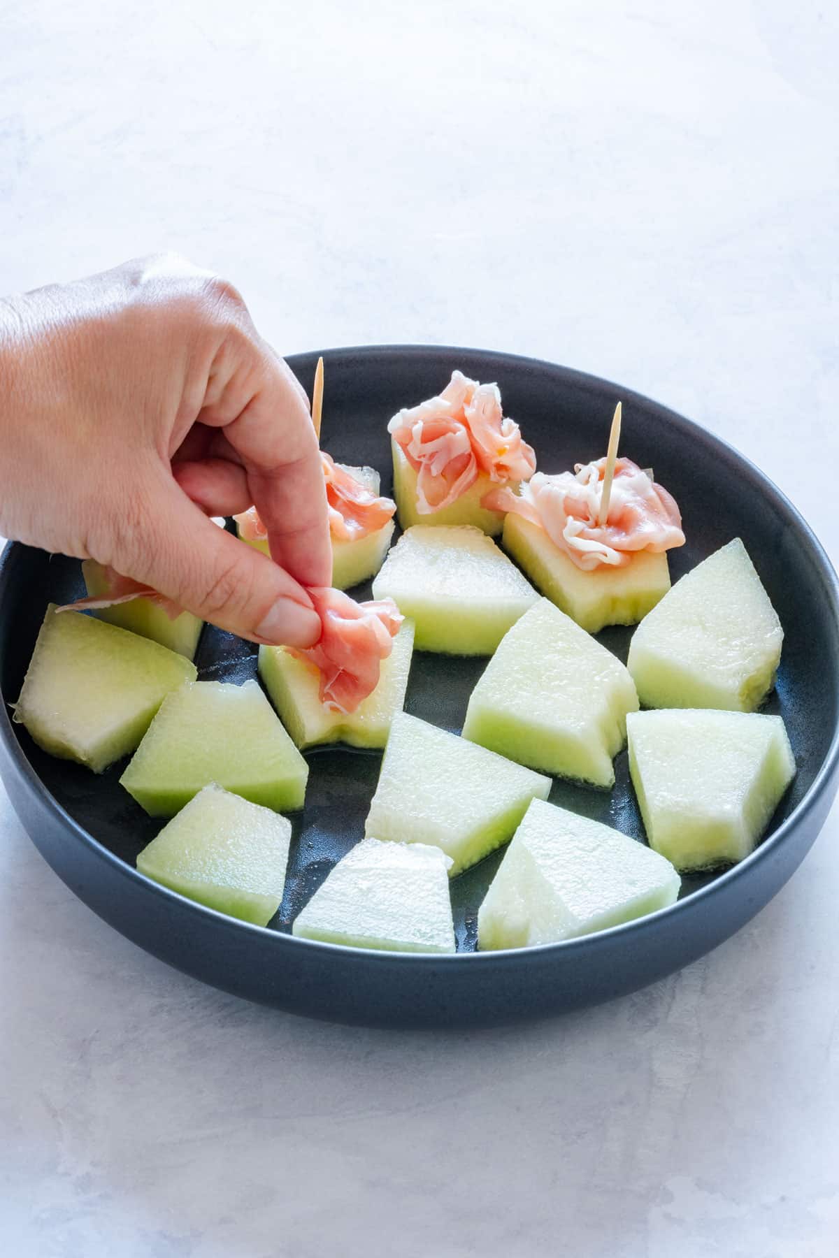 Hand placing prosciutto ham on a piece of melon.