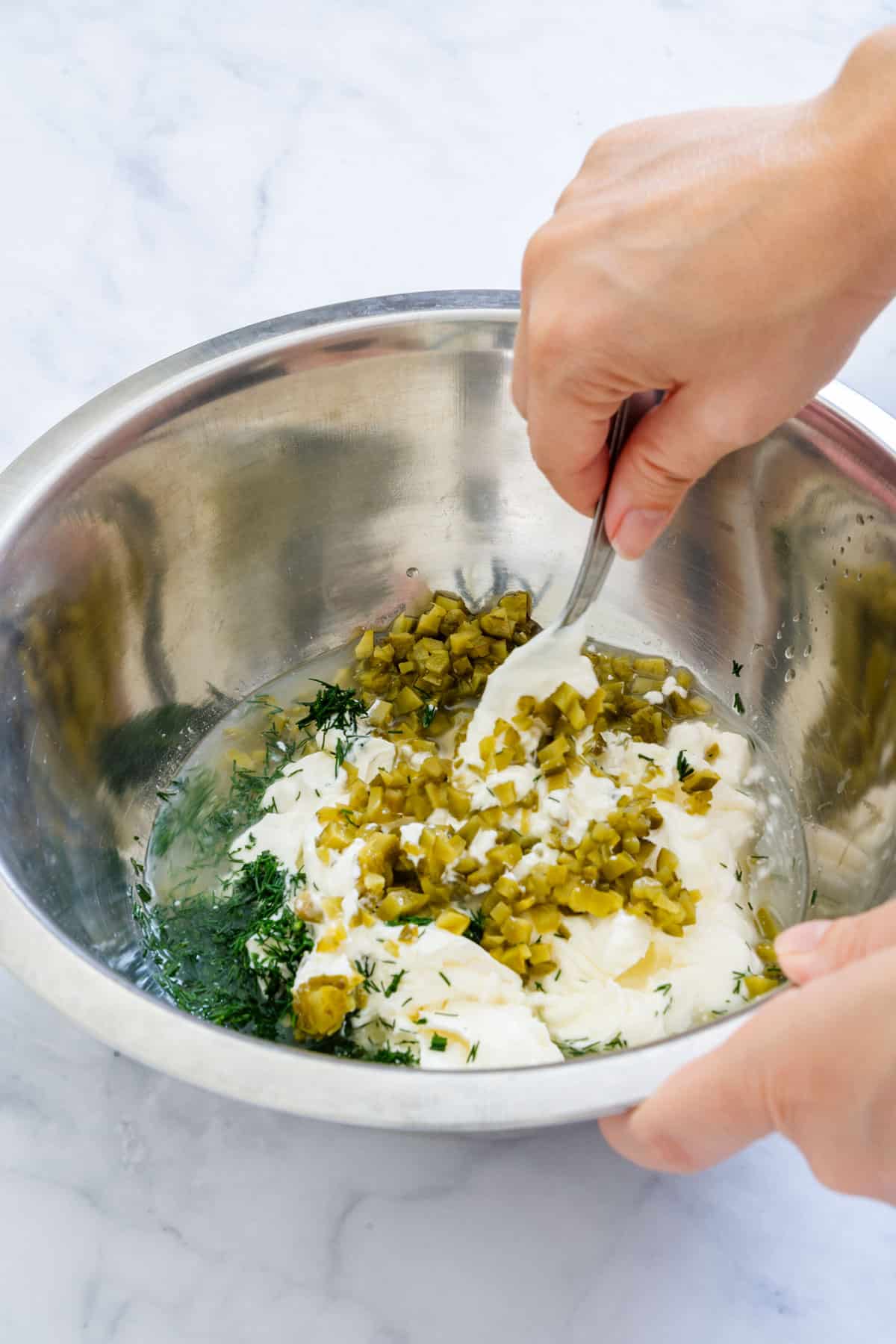 Mixing dill pickles with cream cheese, sour cream and fresh dill.