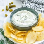 Small bowl of dill pickle dip with potato chips and fresh dill.