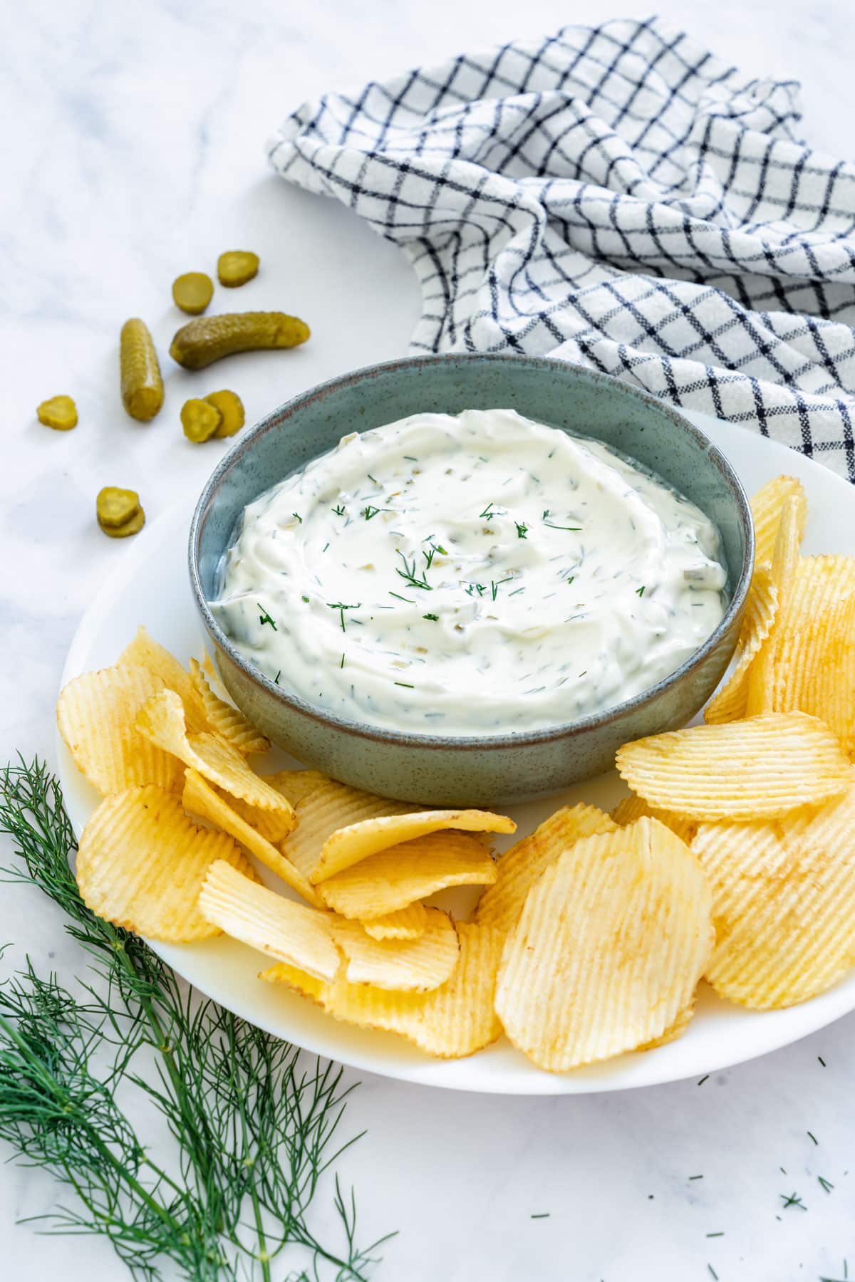 Small bowl of dill pickle dip with potato chips and fresh dill.