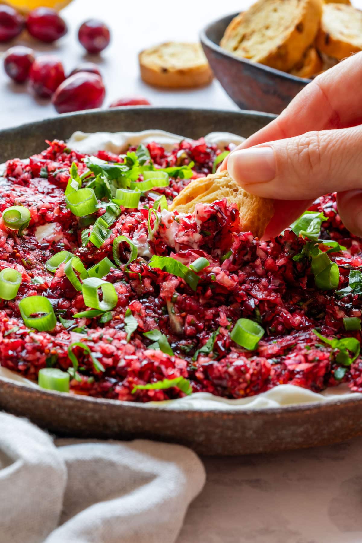 A hand dips bread into cranberry cream cheese dip garnished with green onions.