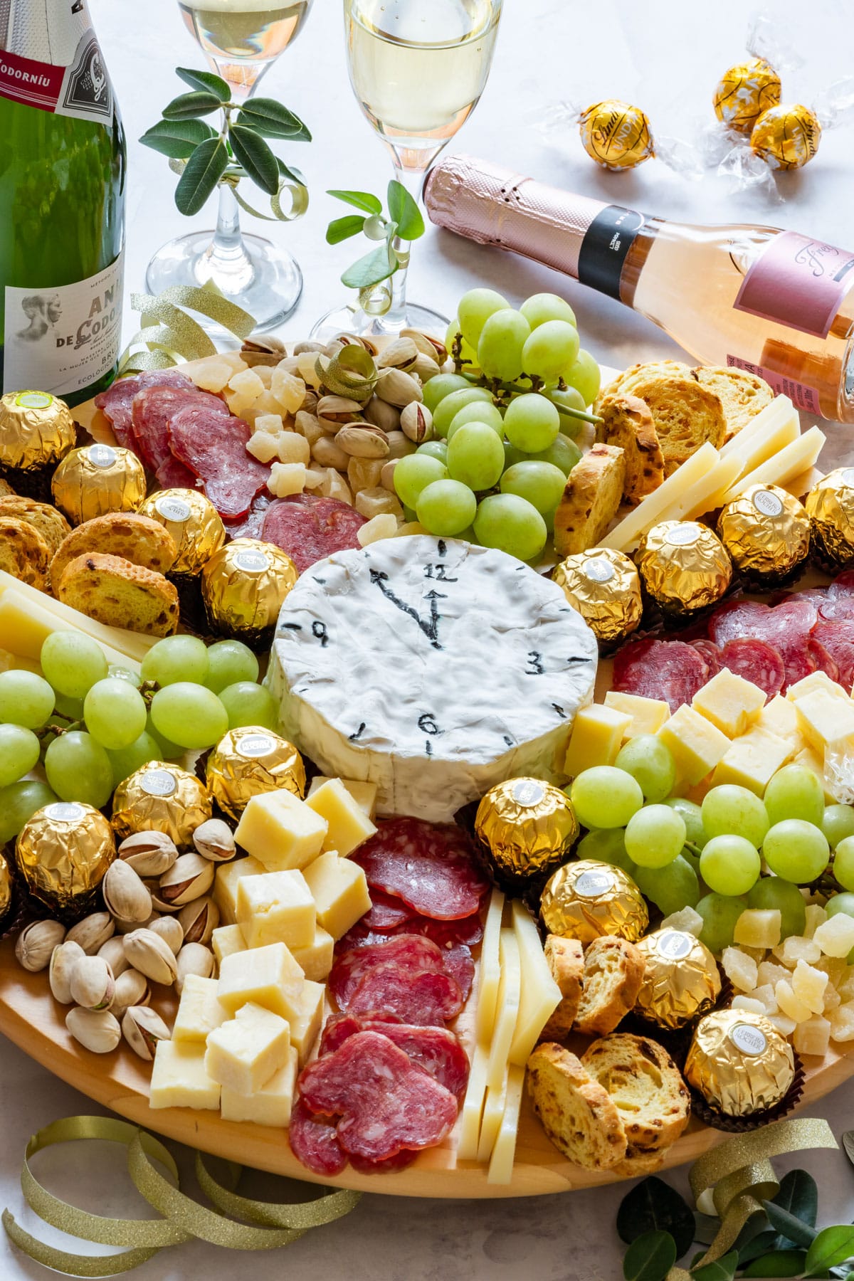 Cheese platter with grapes, salami, chocolates, nuts and wine. Cheese shaped like a clock.