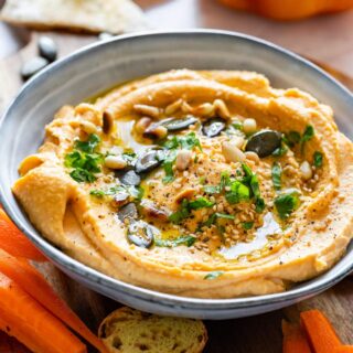 Homemade pumpkin hummus topped with green pumpkin seeds and herbs.