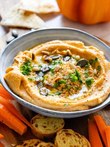 Homemade pumpkin hummus topped with green pumpkin seeds and herbs.