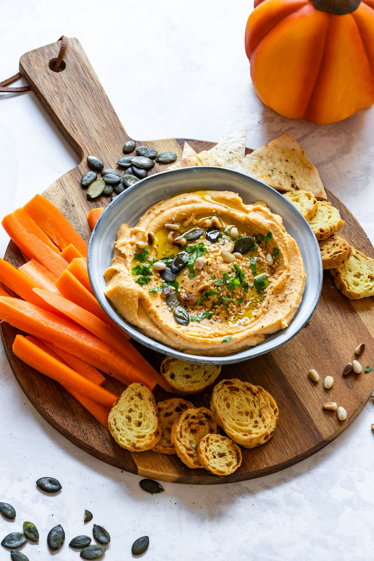 Hummus is placed on a wooden serving board along with carrot sticks and toasted bread slices.