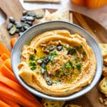 A bowl of hummus garnished with seeds, herbs and a drizzle of olive oil.