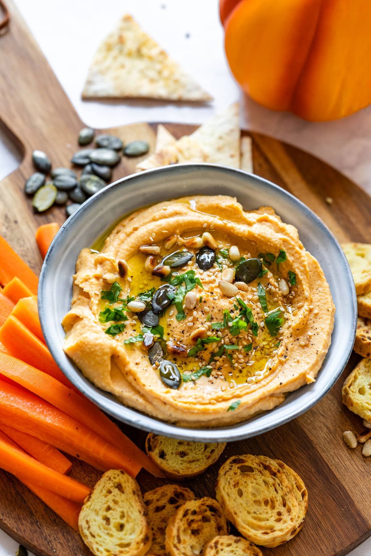 A bowl of hummus garnished with seeds, herbs and a drizzle of olive oil.