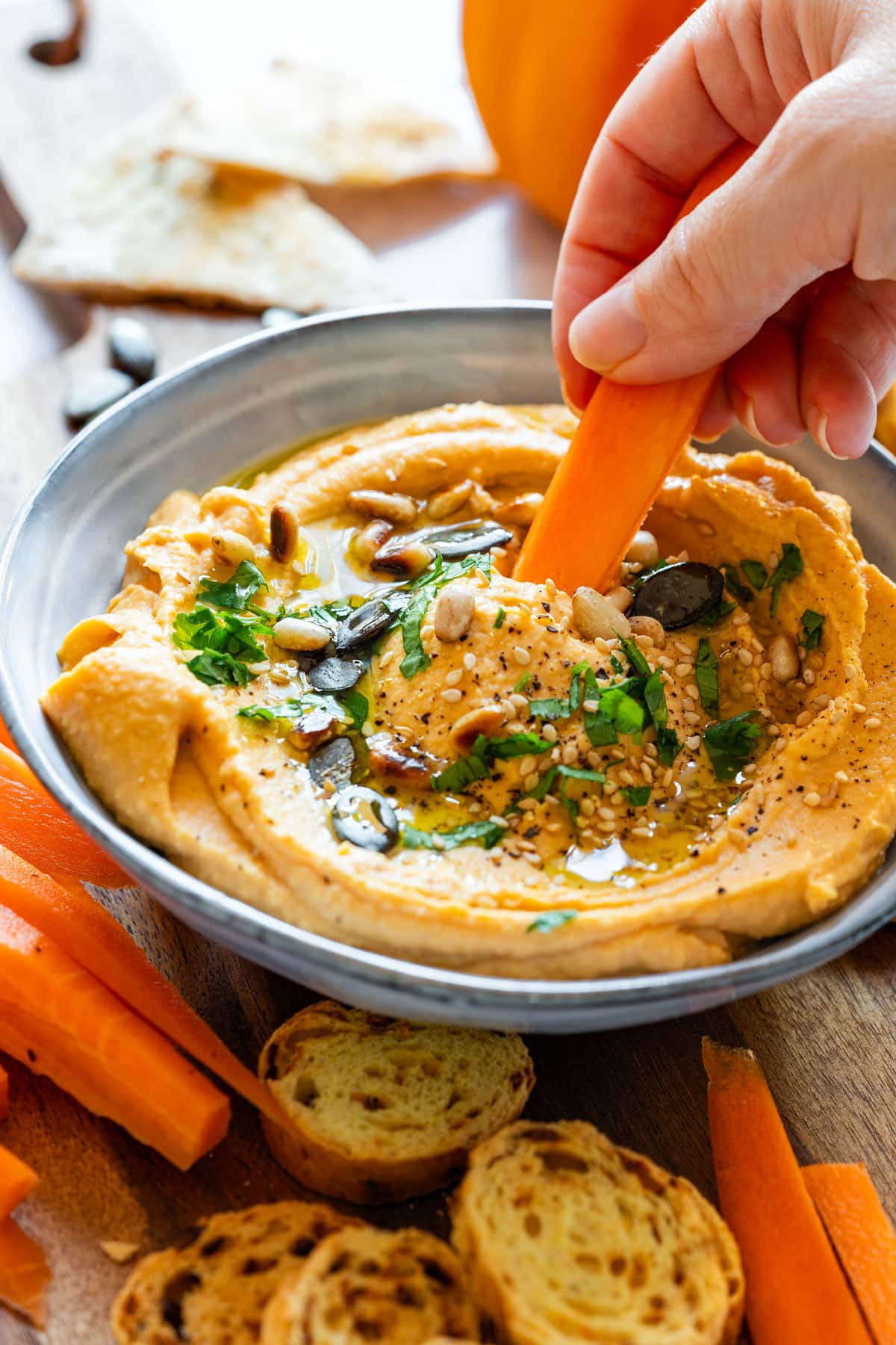 Hand is dipping a carrot stick into the hummus.