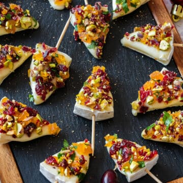 Festive brie Christmas trees appetizers, topped with dried fruits and nuts, arranged on a slate board.