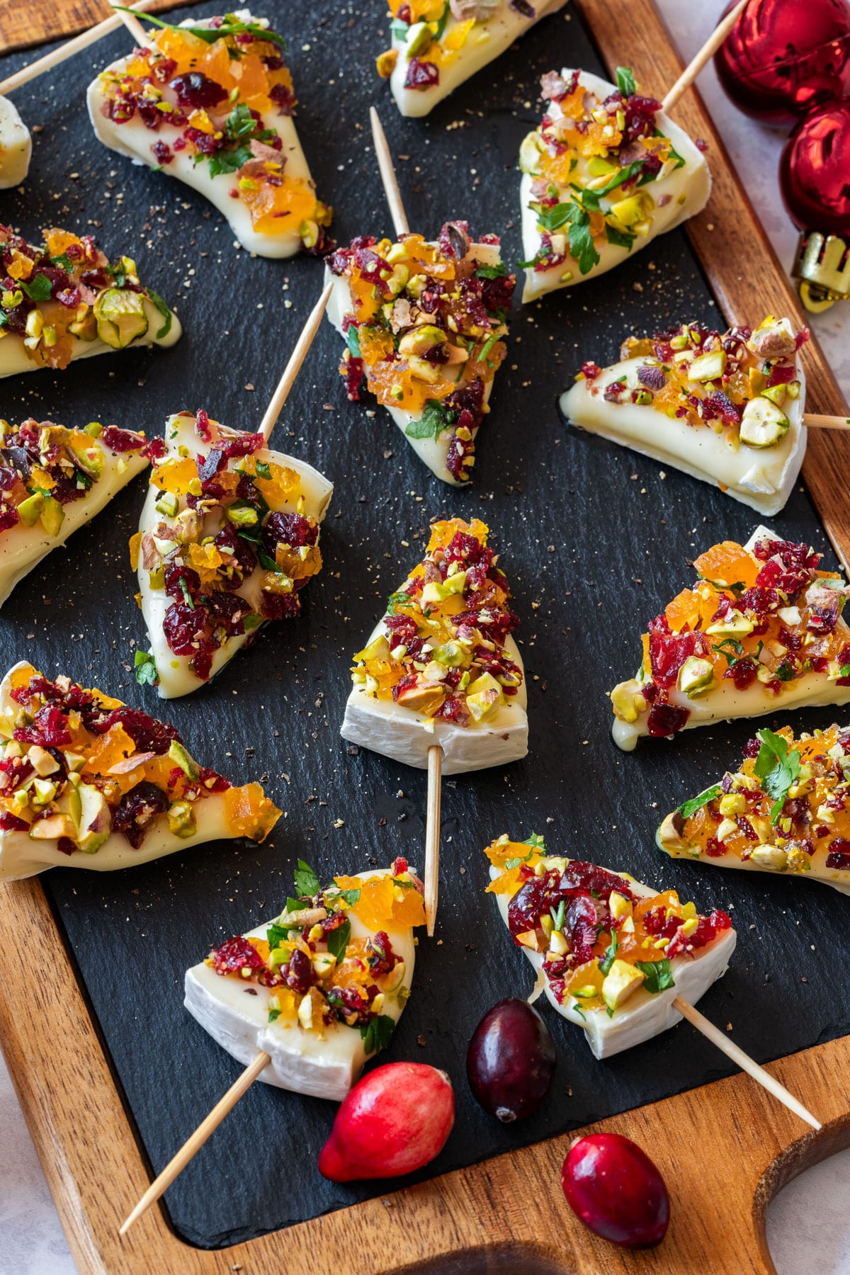 Festive brie Christmas trees appetizers, topped with dried fruits and nuts, arranged on a slate board.