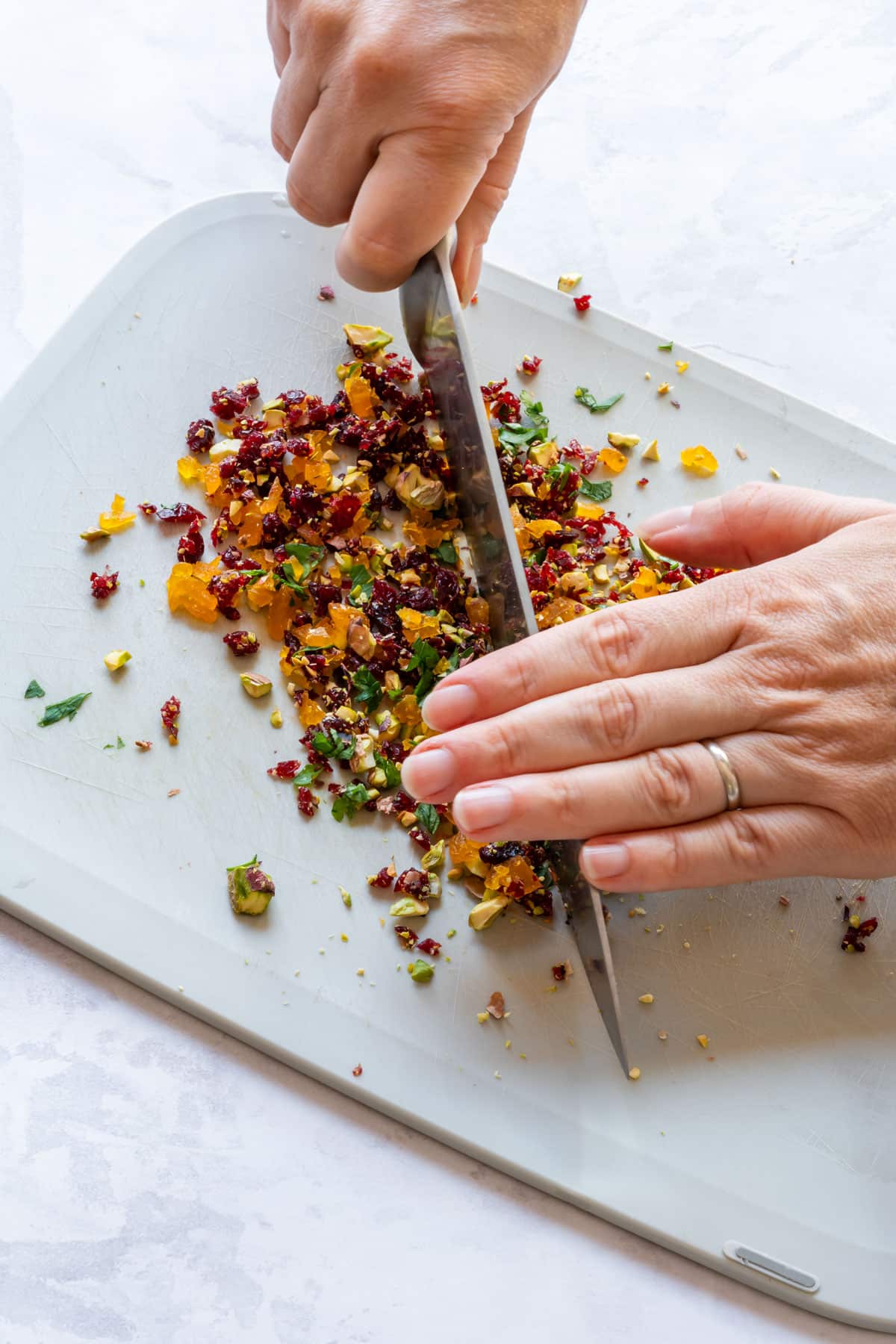 Julia is chopping a mixture of dried fruits and pistachios on a cutting board with a large knife.