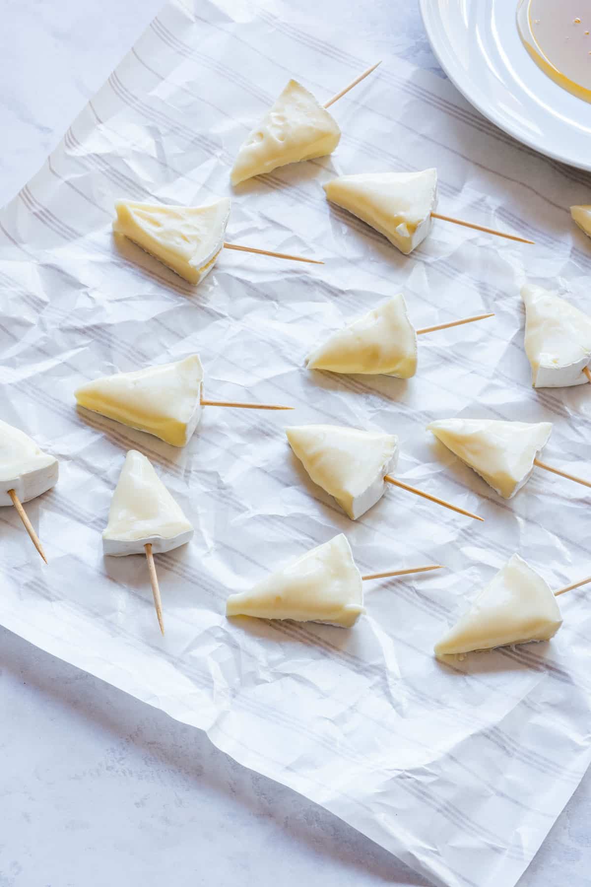 Christmas tree-shaped Brie on toothpicks, arranged on parchment paper.