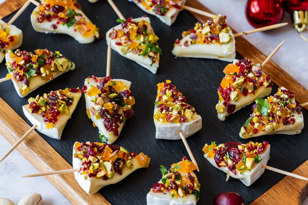 Christmas tree-shaped cheese pieces on toothpick, topped with chopped nuts and dried fruits.