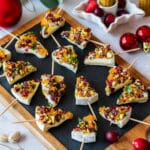 Festive Christmas tree-shaped appetizers with cheese, nuts and dried fruits on skewers, arranged on a slate board.