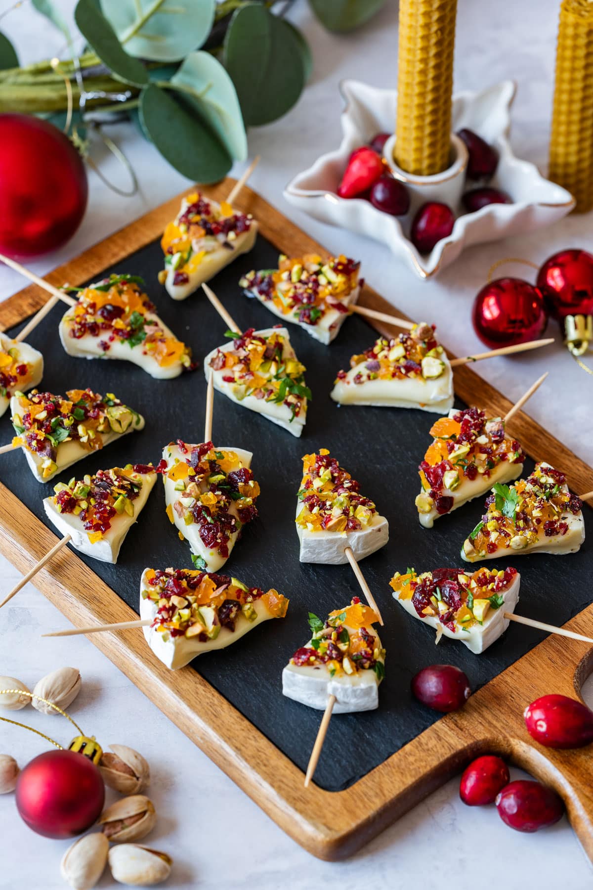 Festive Christmas tree-shaped appetizers with cheese, nuts and dried fruits on skewers, arranged on a slate board.