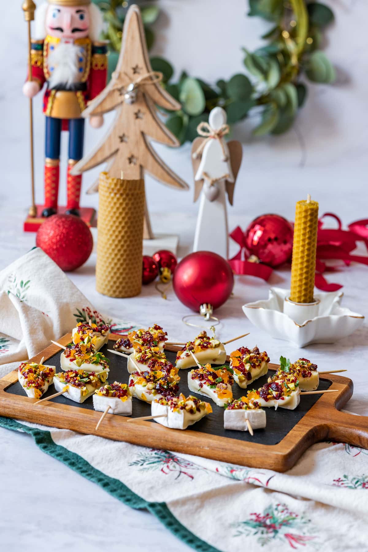 A festive holiday scene with a nutcracker, wooden decorations, candles and a tray of fancy brie cheese appetizers.