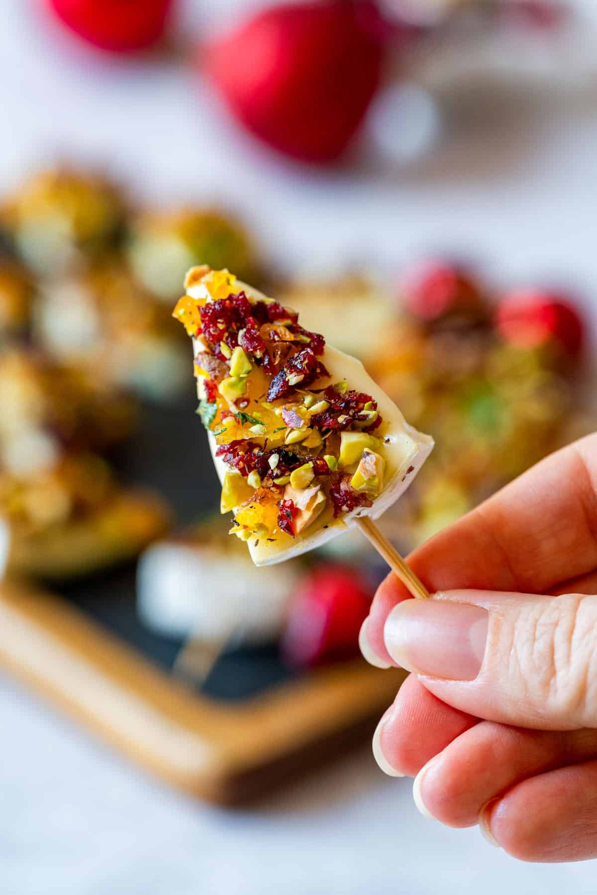 Julia holds a mini brie Christmas tree topped with chopped nuts and dried fruits on a toothpick.