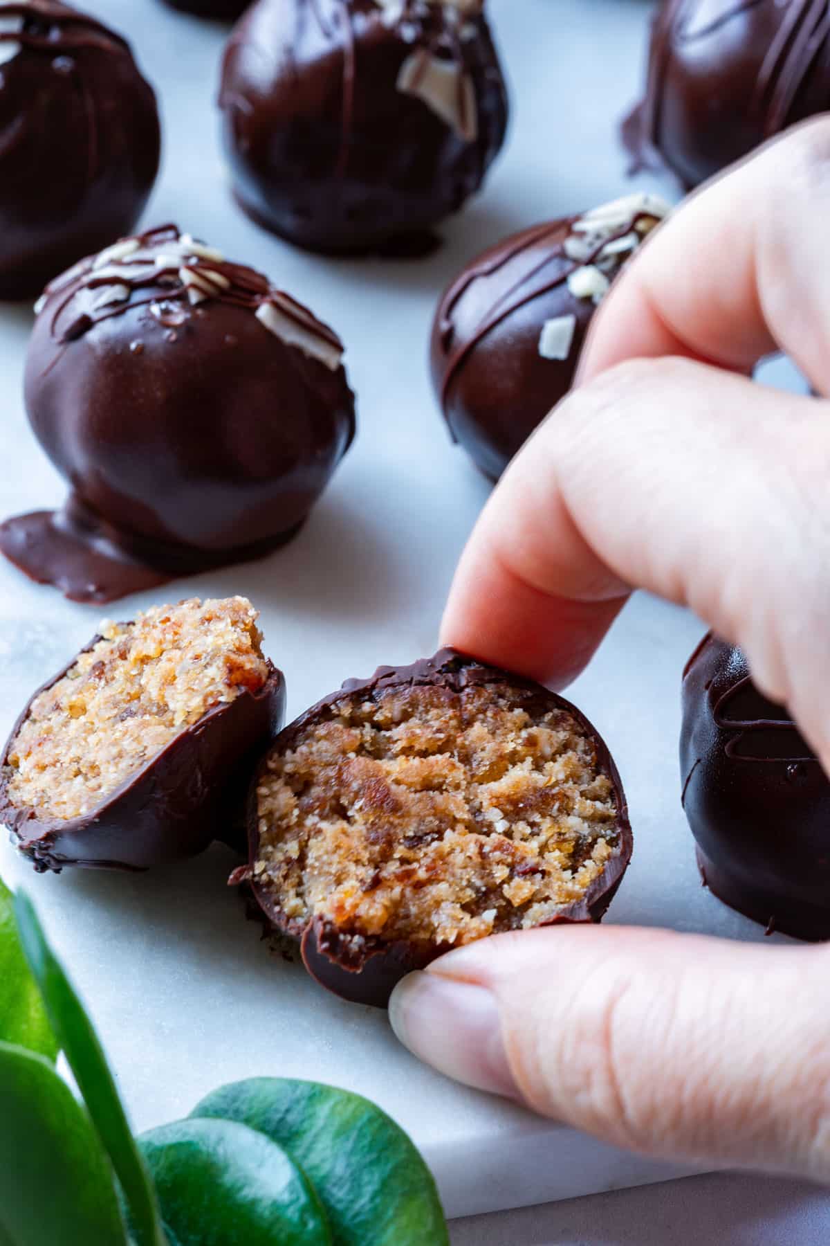 A hand is taking chocolate-covered truffles, one open to reveal its filling.