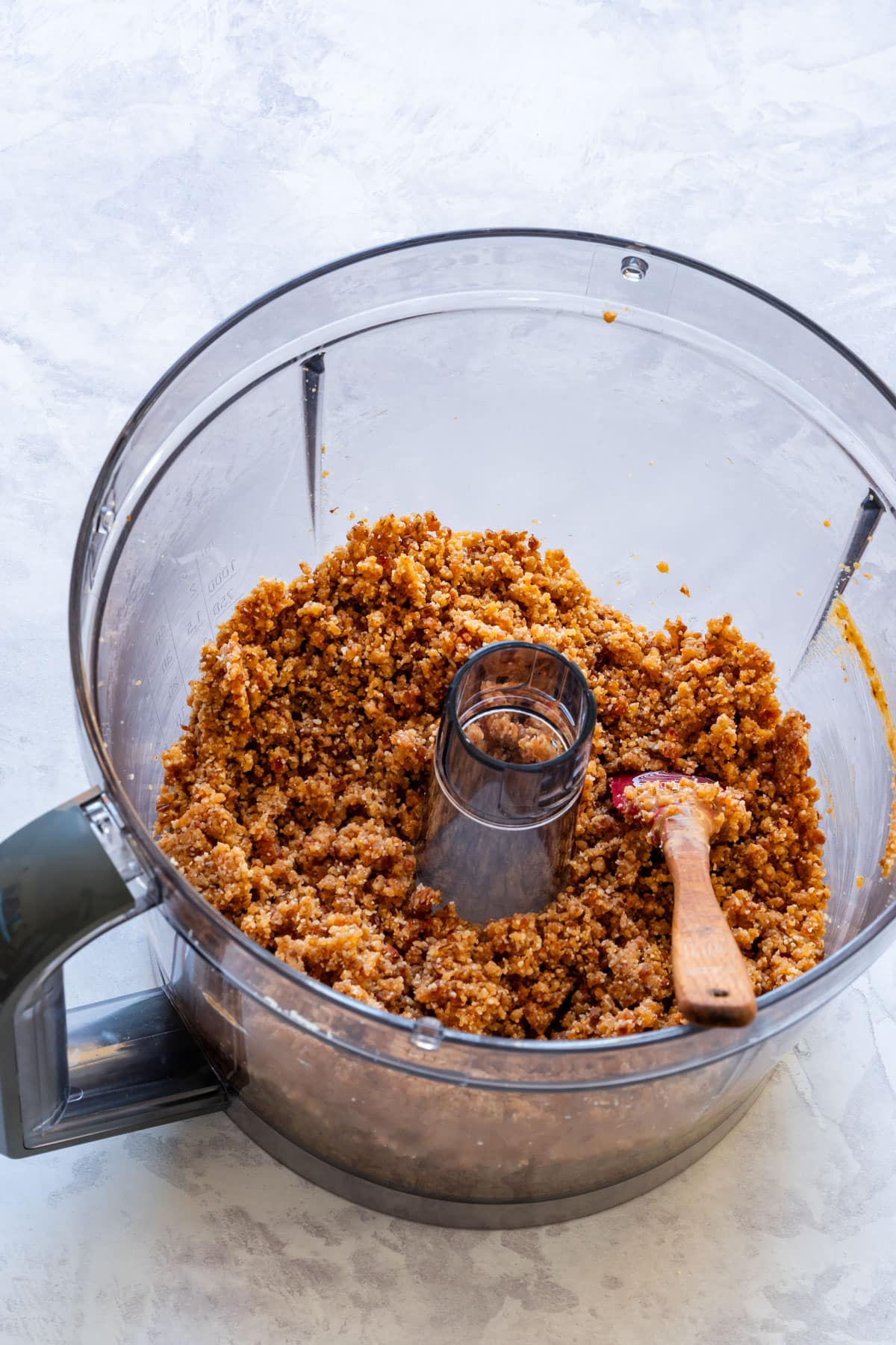 A food processor bowl filled with a crumbly truffle mixture and a wooden spoon inside.