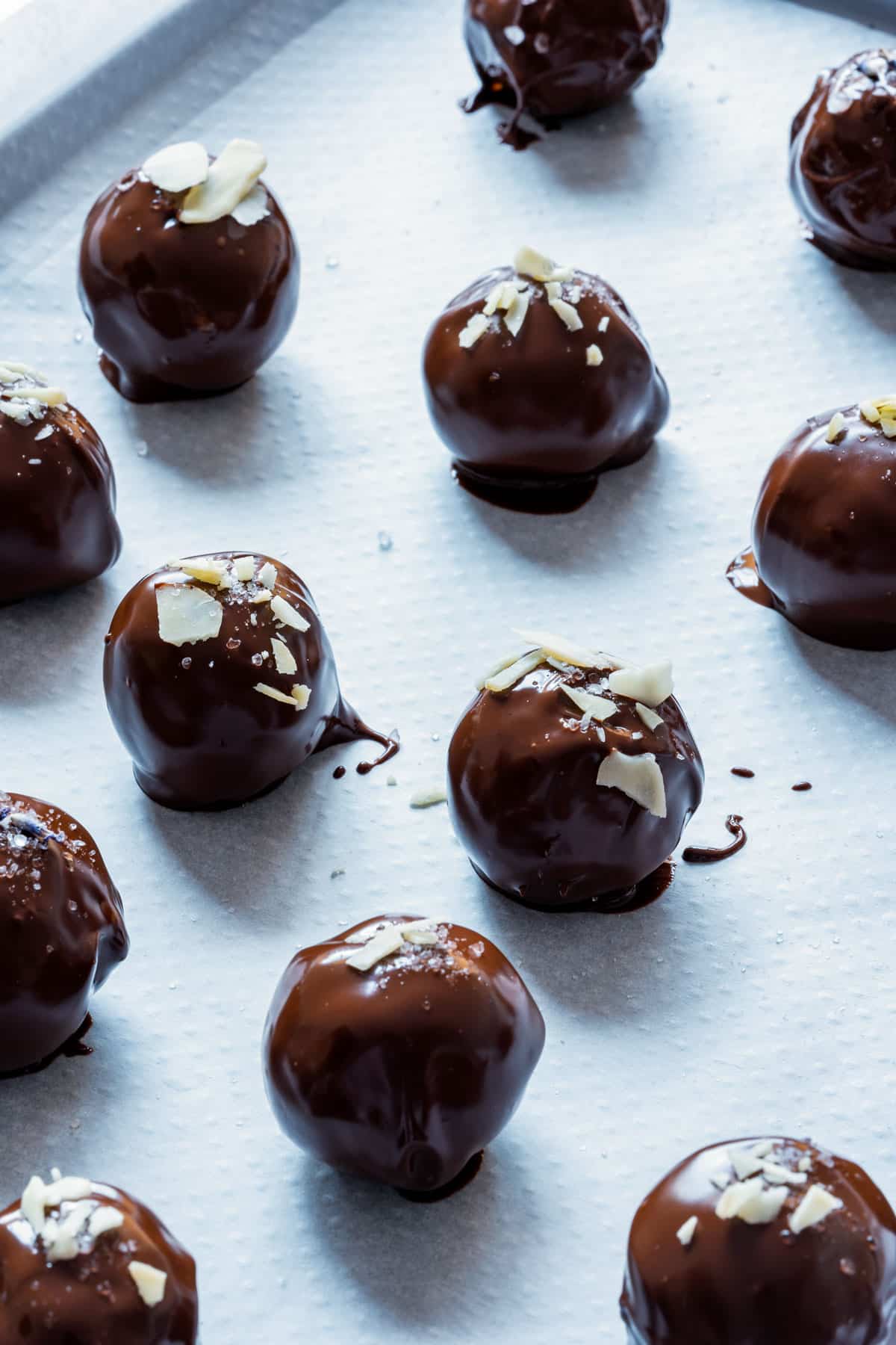 Chocolate truffles topped with almond slices on a parchment-lined baking sheet.