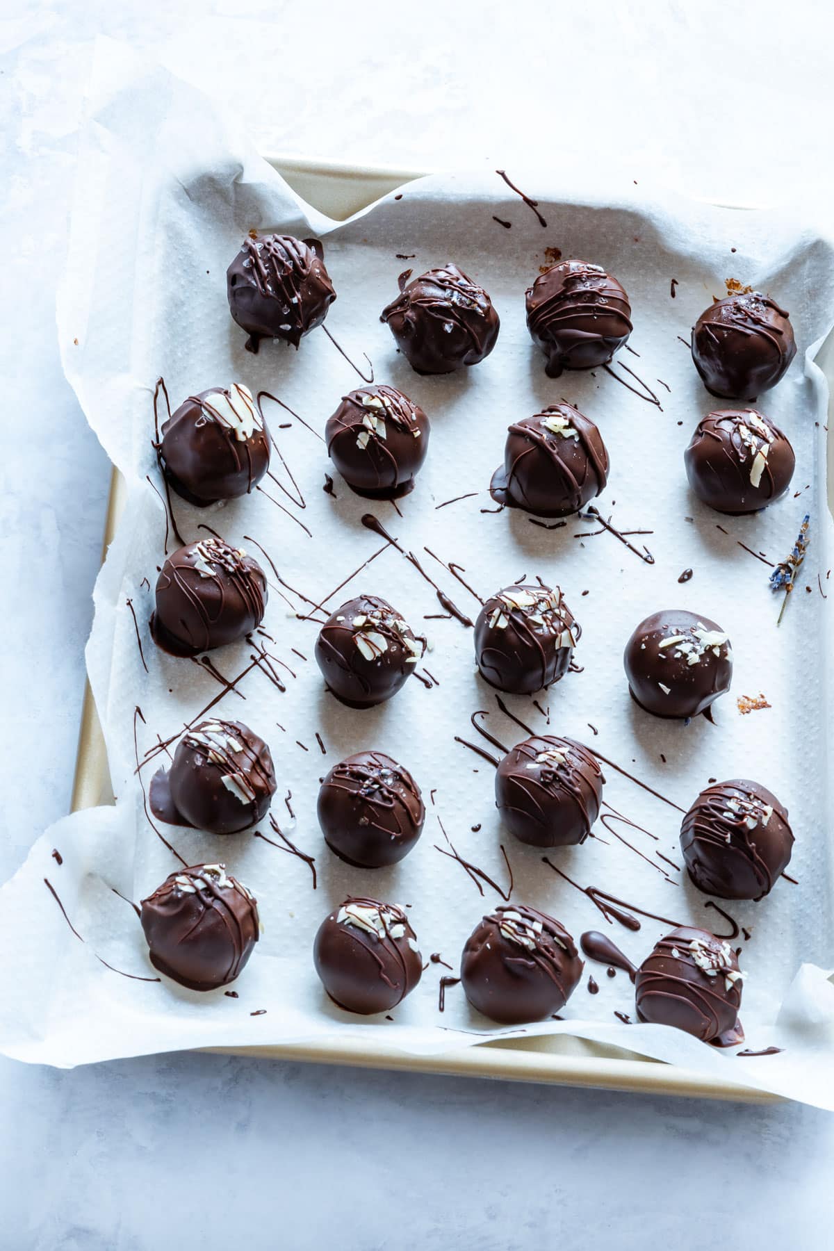 Chocolate truffles on a parchment-lined tray, drizzled with chocolate and topped with almond slices.