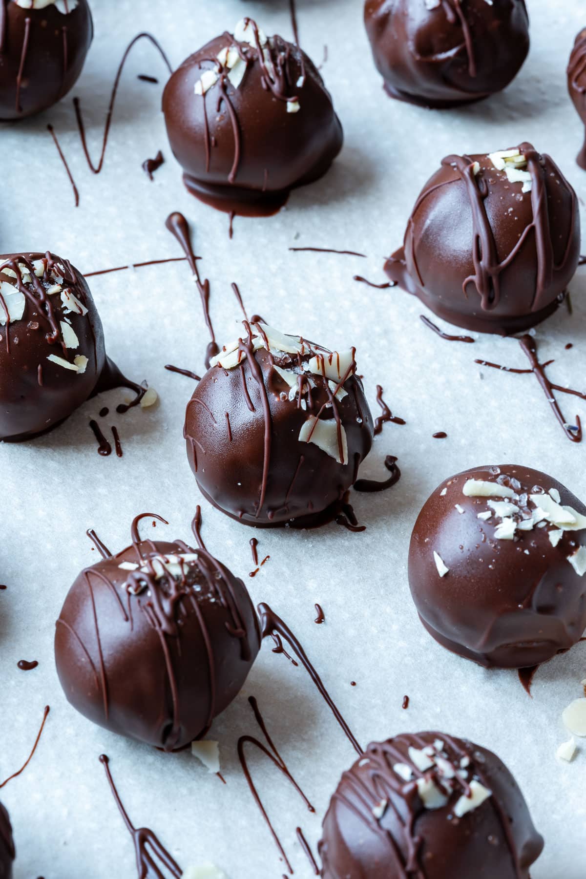 Luxurious chocolate truffles with drizzled chocolate and almond flakes on parchment paper.