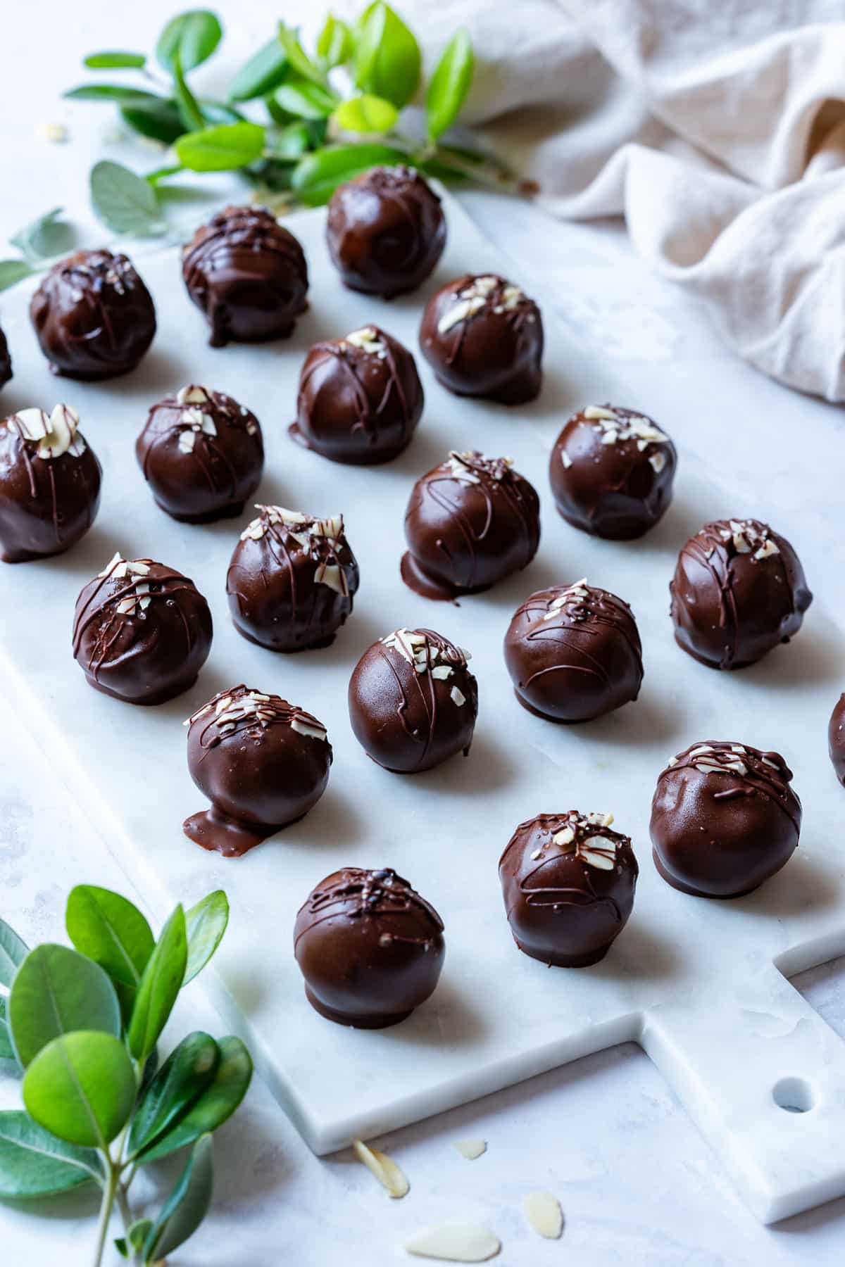 Chocolate truffles lined on a marble board, garnished with almond slices and drizzled with chocolate.