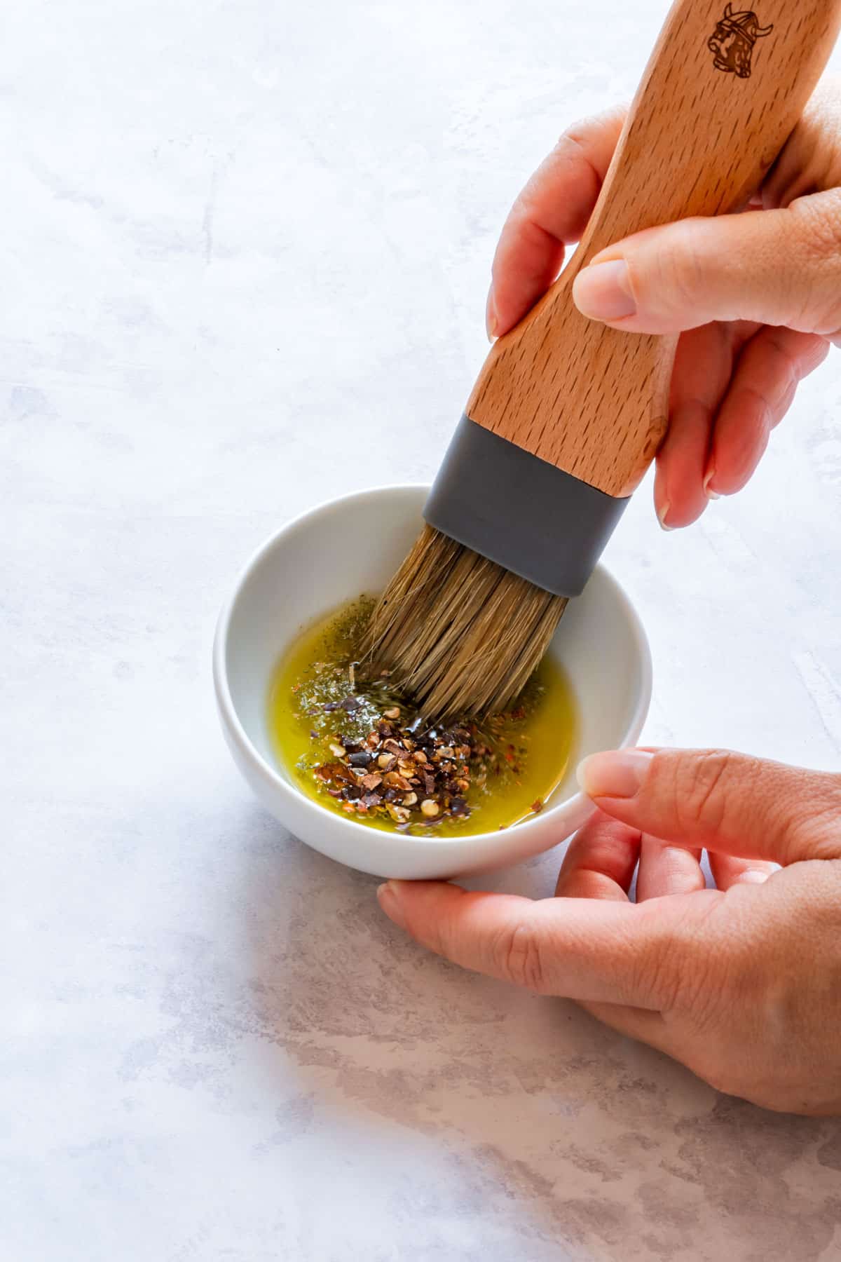 Julia holds a brush dipping into a tiny bowl of oil mixed with chili flakes.