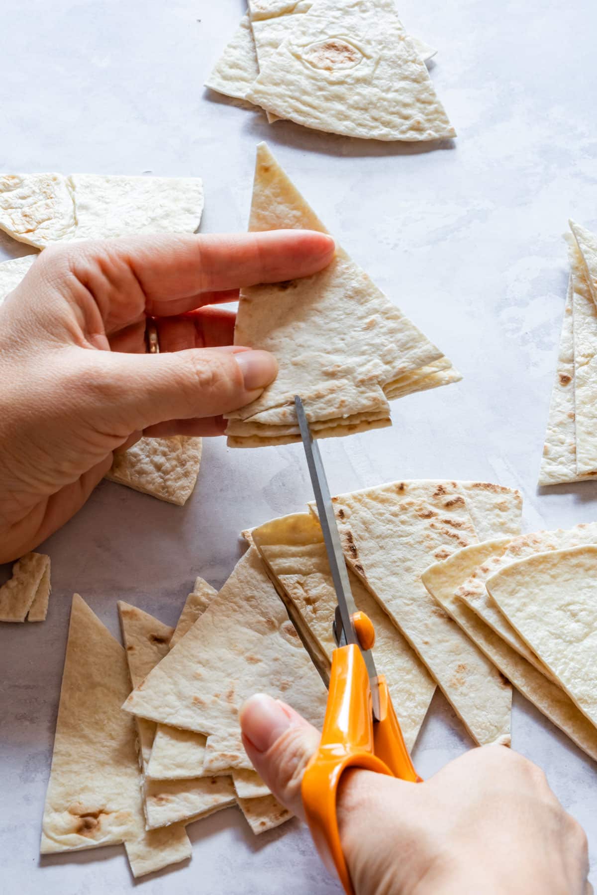 Julia is cutting tortilla pieces into Christmas tree-shapes with orange-handled scissors.