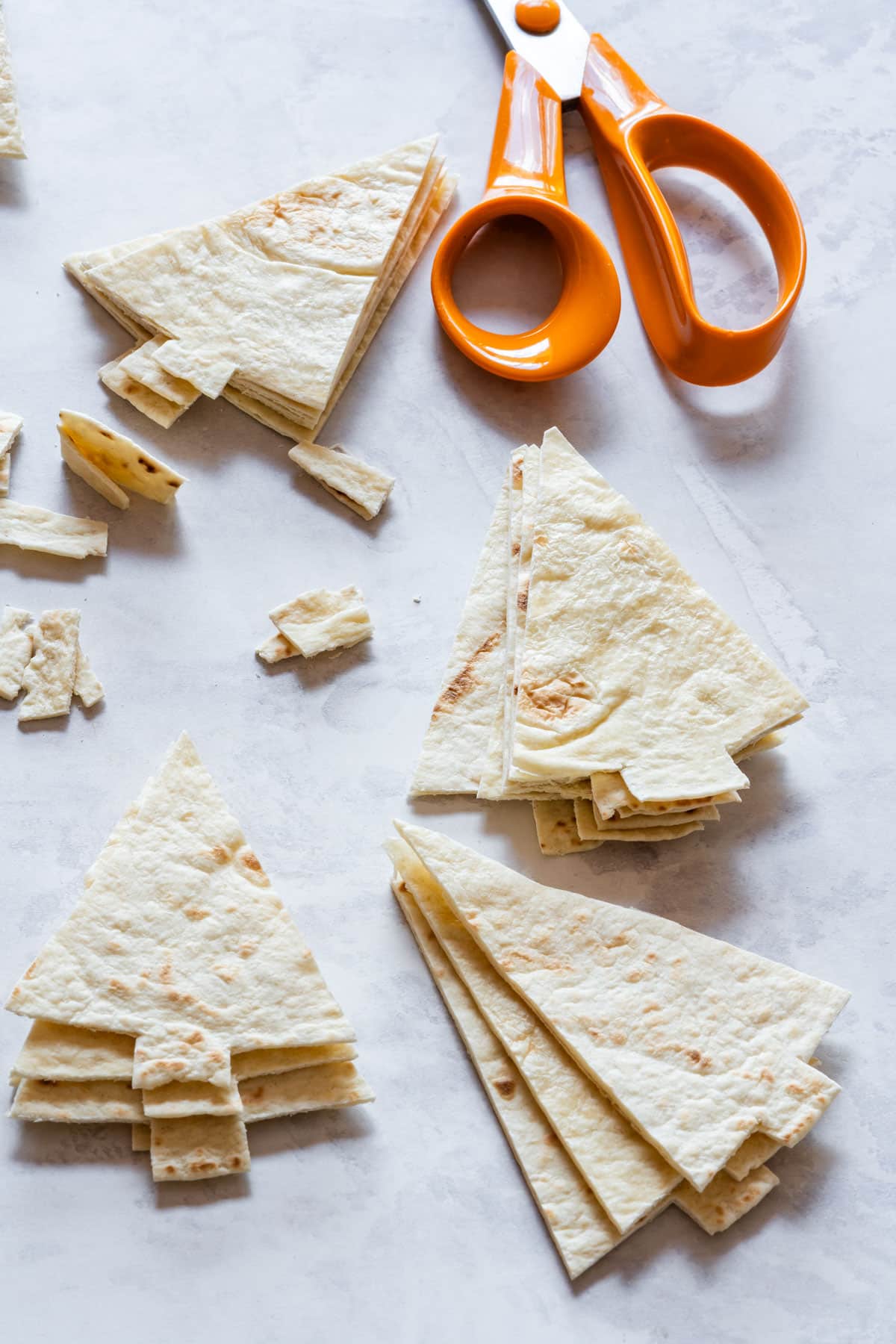 Tortilla pieces cut into Christmas tree-shapes with orange-handled scissors nearby.