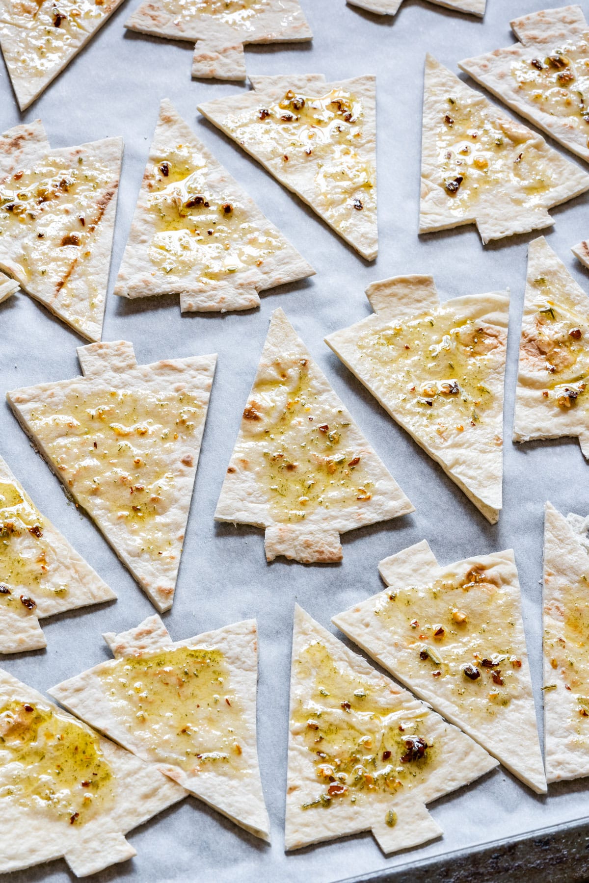 Christmas tree-shaped tortillas with oil and herbs on parchment paper, ready for baking.