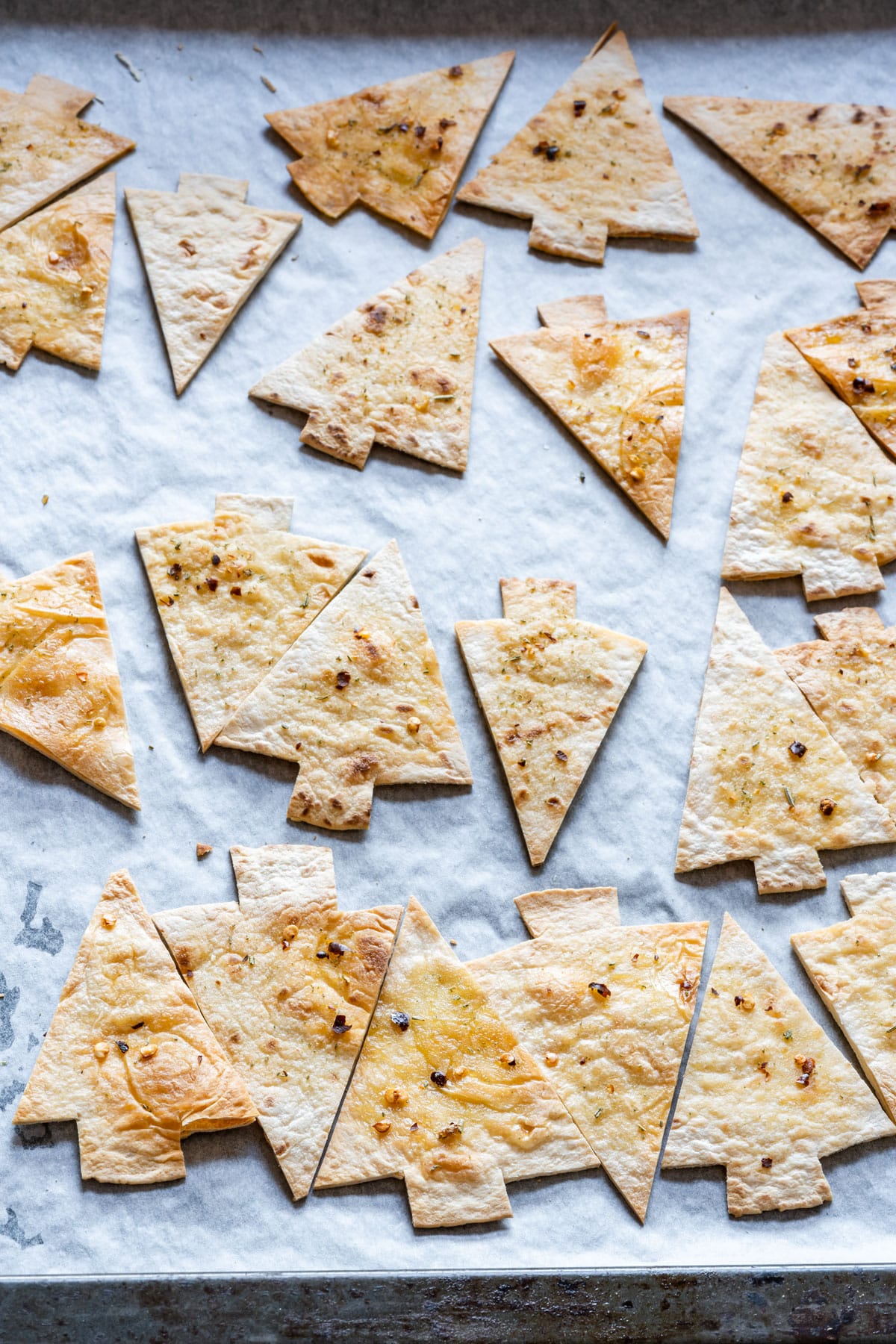 Baked tortilla chips cut into Christmas tree shapes, seasoned and placed on parchment paper.