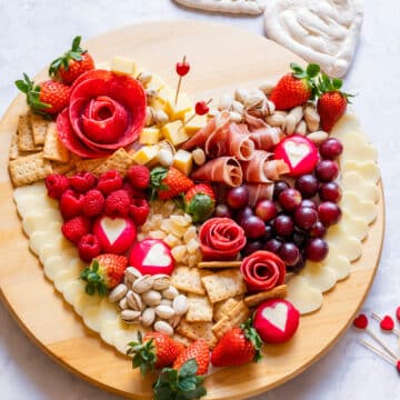 A heart-shaped Valentine's Day charcuterie board featuring cheese, meats, strawberries, raspberries, grapes, crackers and nuts.