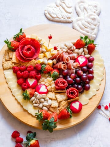 A heart-shaped Valentine's Day charcuterie board featuring cheese, meats, strawberries, raspberries, grapes, crackers and nuts.