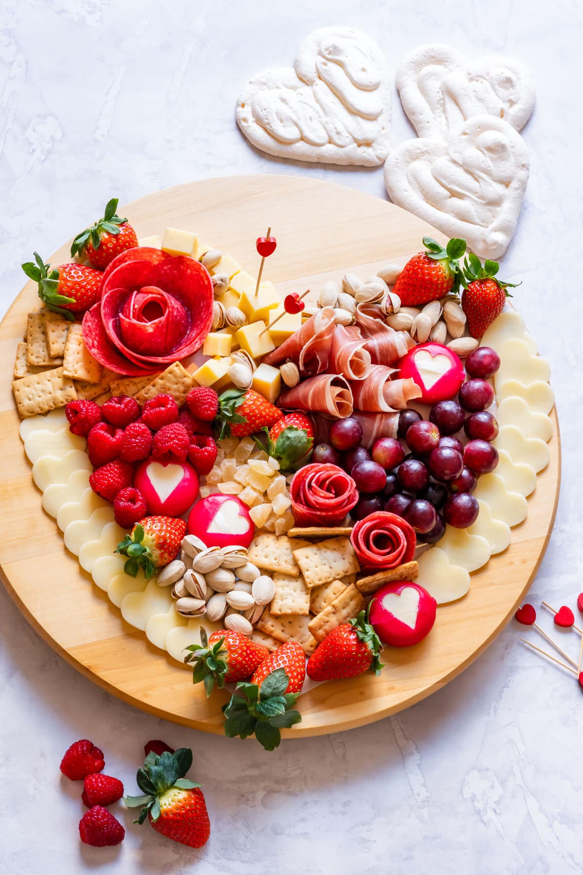 A heart-shaped Valentine's Day charcuterie board featuring cheese, meats, strawberries, raspberries, grapes, crackers and nuts.