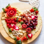 Romantic heart-shaped charcuterie board with red berries, meats, cheese, crackers and nuts.