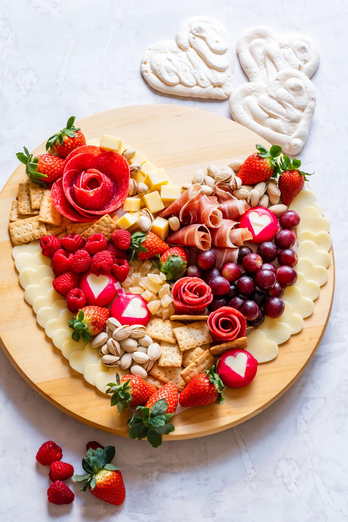 Romantic heart-shaped charcuterie board with red berries, meats, cheese, crackers and nuts.