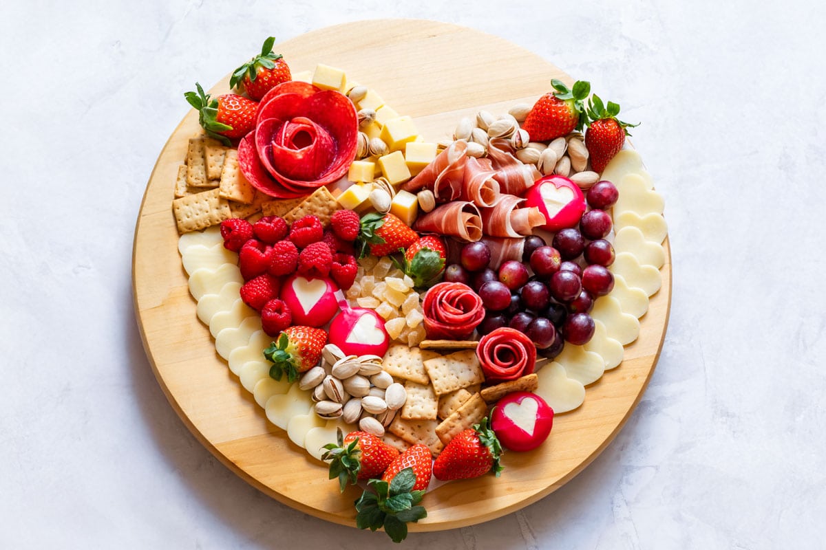 Heart-shaped charcuterie board with salami roses, prosciutto, cheese and red berries.