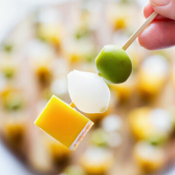 Close-up of an Irish flag appetizer skewer with cheddar cheese, pearl onion and green olive with more skewers in the background.