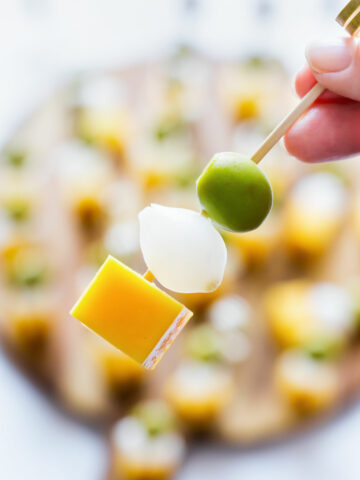 Close-up of an Irish flag appetizer skewer with cheddar cheese, pearl onion and green olive with more skewers in the background.