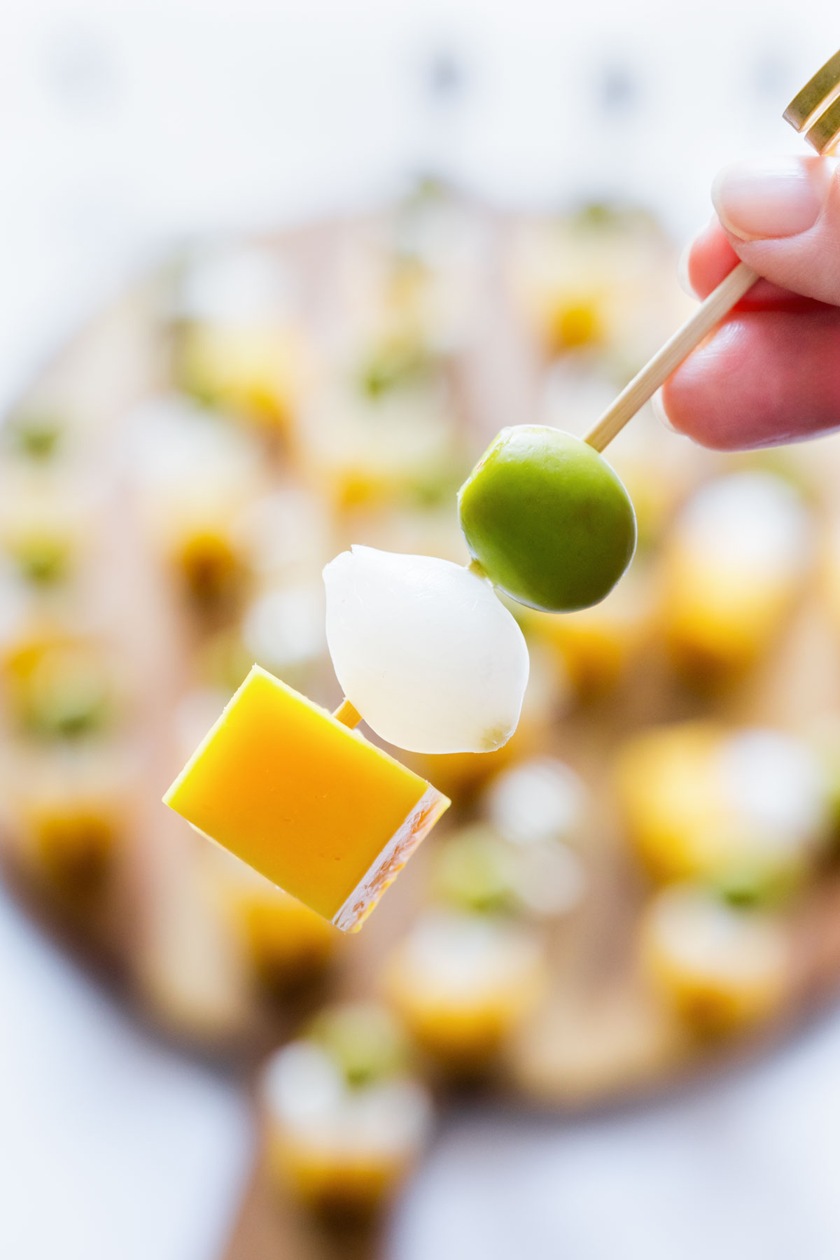 Close-up of an Irish flag appetizer skewer with cheddar cheese, pearl onion and green olive with more skewers in the background.