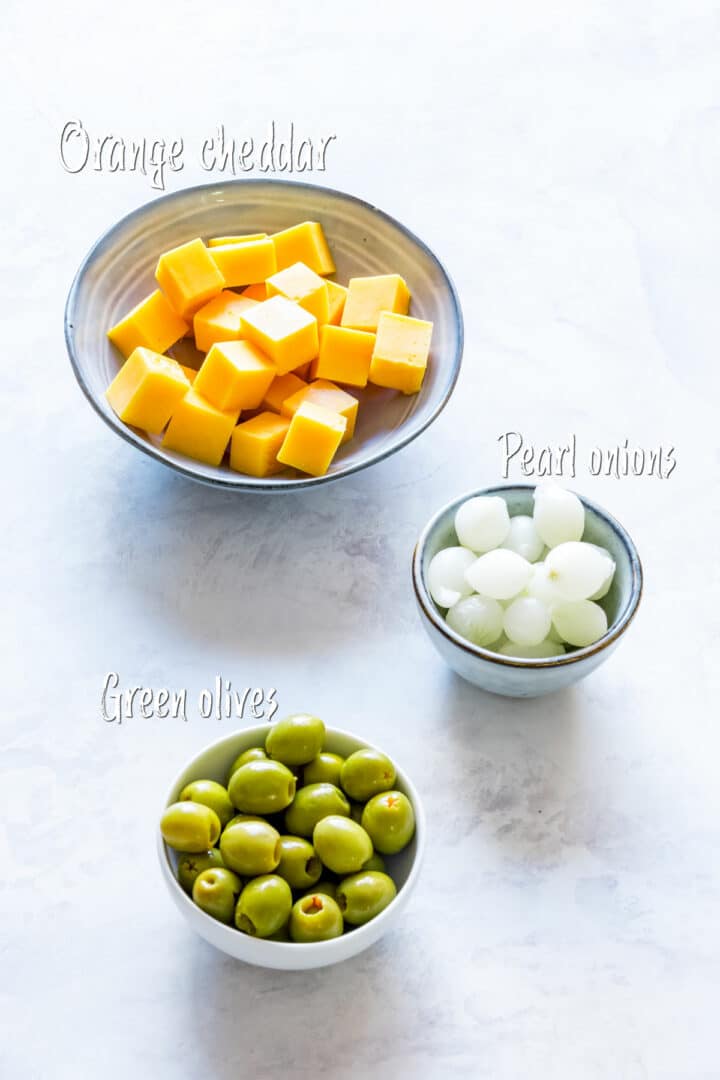 Three small bowls filled with ingredients for Irish-inspired appetizer skewers, displayed on a light surface.